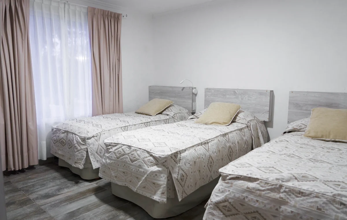 Habitación con 3 camas individuales y ventana con cortinas, correspondientes a la Casa 1