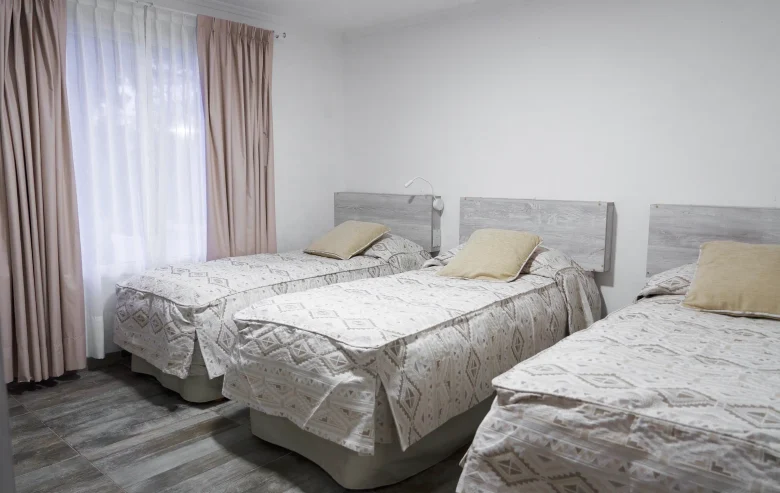Habitación con 3 camas individuales y ventana con cortinas, correspondientes a la Casa 1