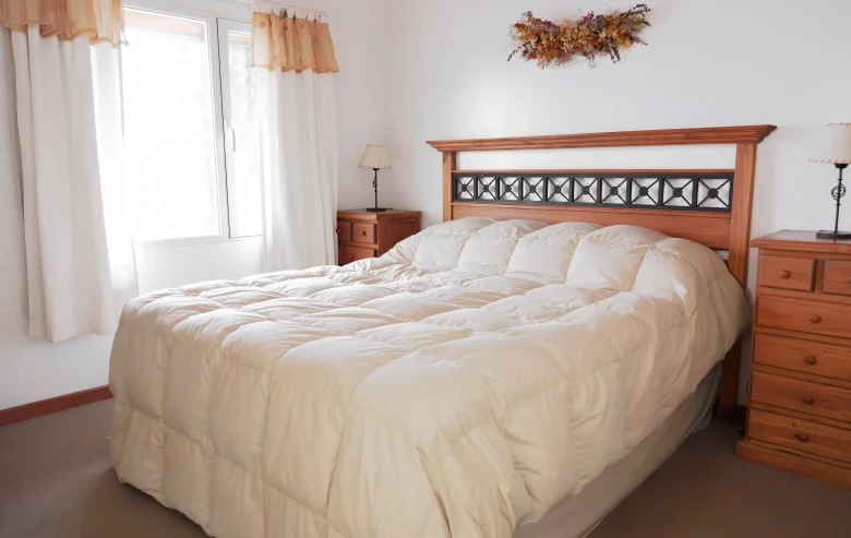 Dormitorio principal con cama matrimonial, acolchado de pluma, mesitas de luz y veladores con ventana y cortinas, correspondiente a la Casa 2