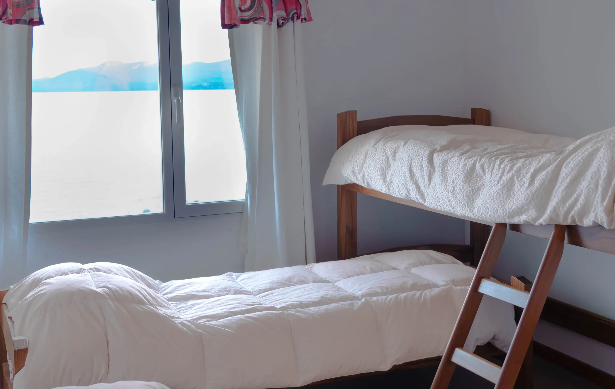 Dormitorio secundario con cuchetas cruzadas y ventana con vista al lago y cortinas, correspondiente a la Casa 2