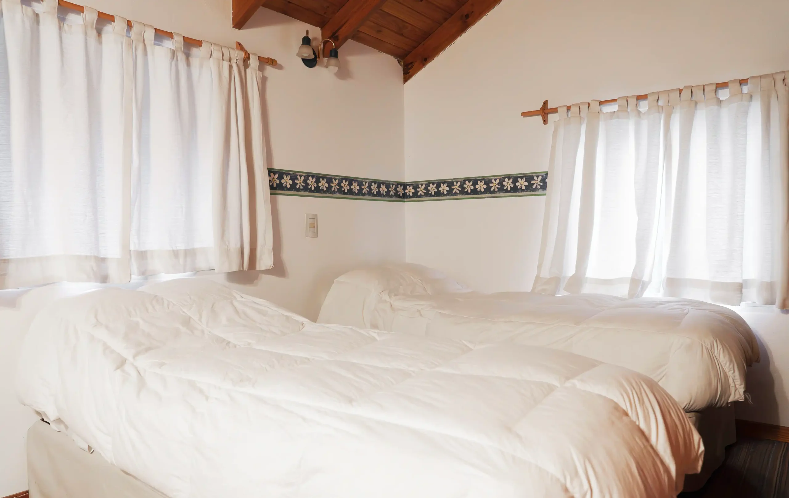 Dormitorio secundario con 2 camas individuales y acolchado de pluma y dos ventanas con cortinas, correspondiente a la Casa 4