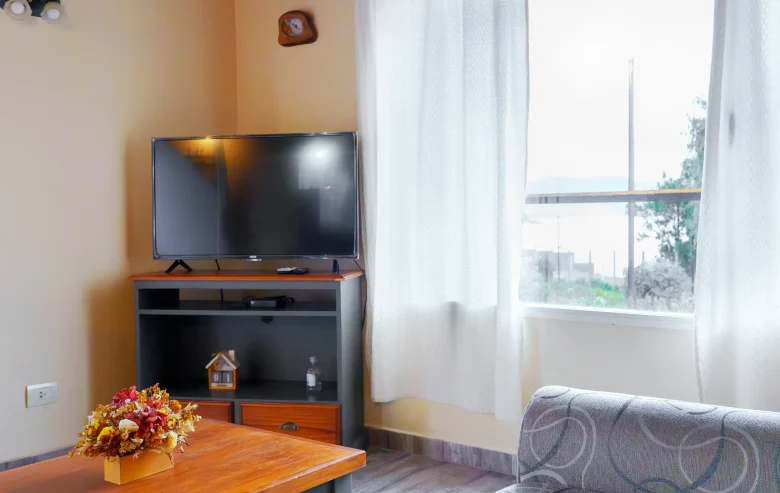 Living con mesa con televisor, ventana y cortinas con vista al lago, correspondiente a la Casa 4