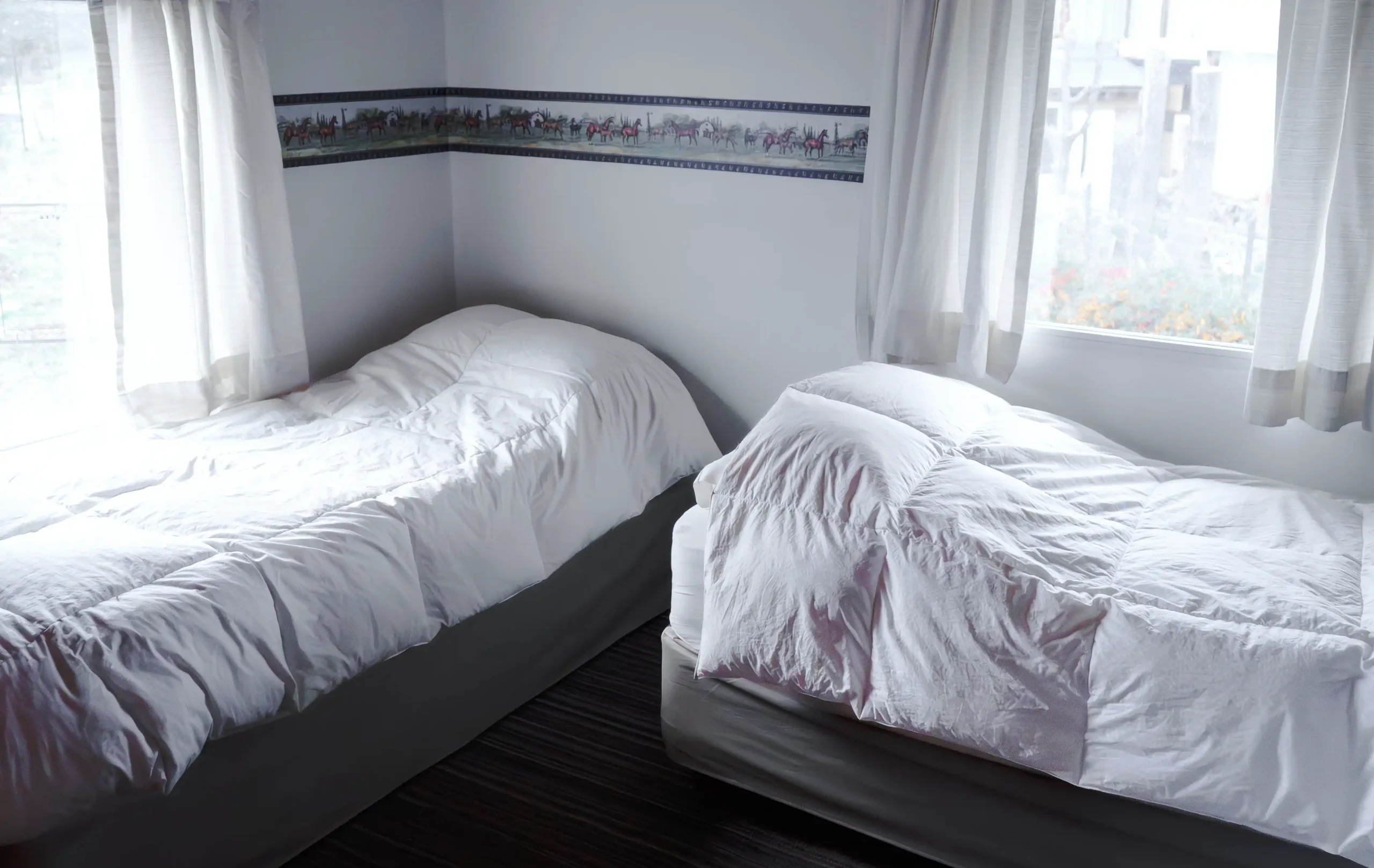 Dormitorio secundario con dos camas individuales y dos ventanas con cortinas, correspondiente a la Casa 5