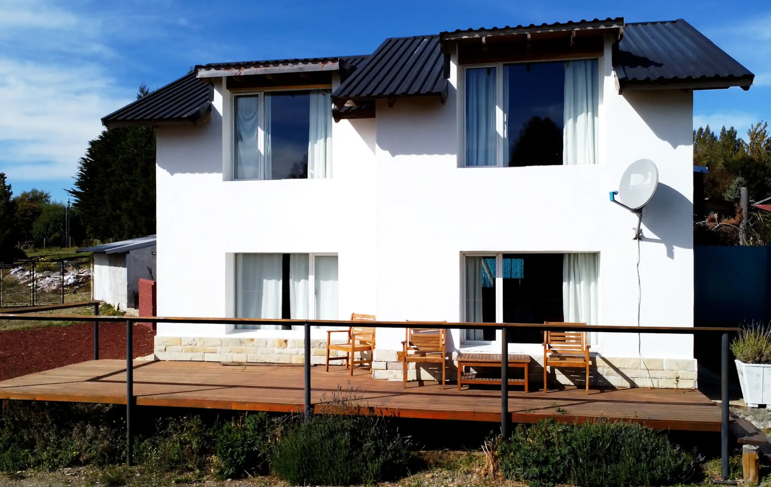 Casa 4 y 5 vistas desde el exterior. Casa grande con 4 ventanas y deck de madera con barandas con sillas y mesa