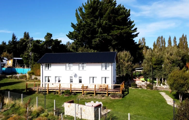 Alojamientos Exclusivos: Casa 2 y 3 vistas desde el exterior. 2 Casas unidas, con 10 ventanas y deck de madera con barandas con sillas y mesa y amplio jardín con parrilla