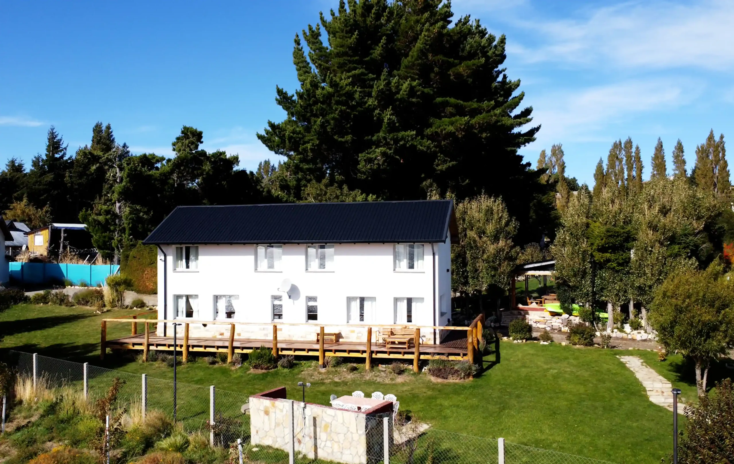 Alojamientos Exclusivos: Casa 2 y 3 vistas desde el exterior. 2 Casas unidas, con 10 ventanas y deck de madera con barandas con sillas y mesa y amplio jardín con parrilla